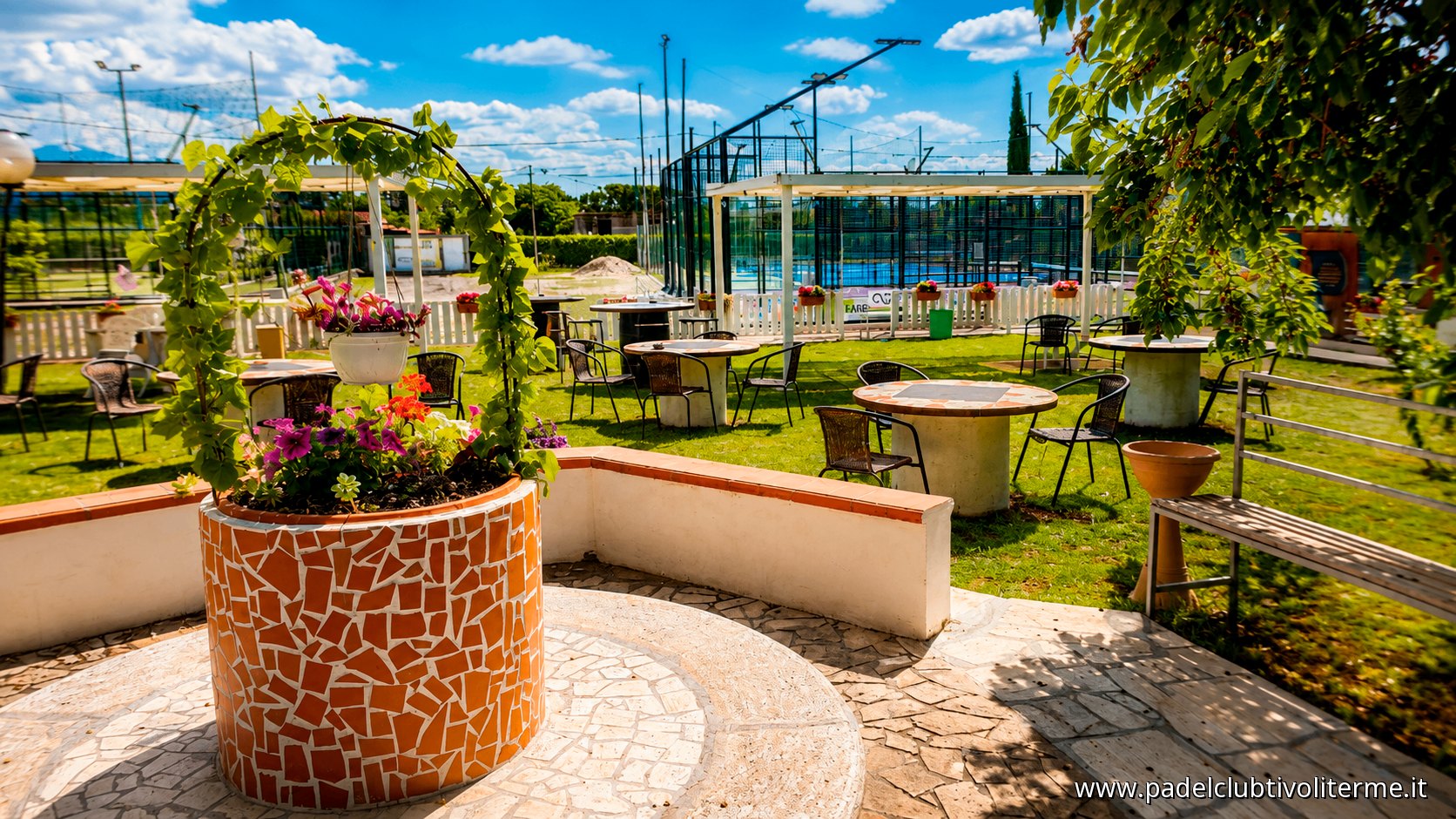 Giardino con arco fiorito e tavoli affacciati sui campi da padel